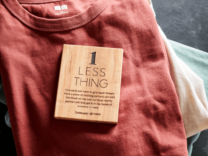 A wooden block captioned One Less Thing sits atop a red folded shirt