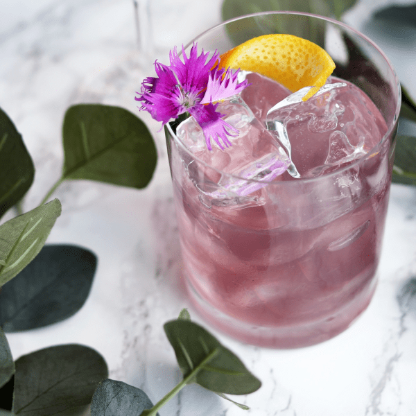 A pink cocktail with a lemon wedge and flower garnish