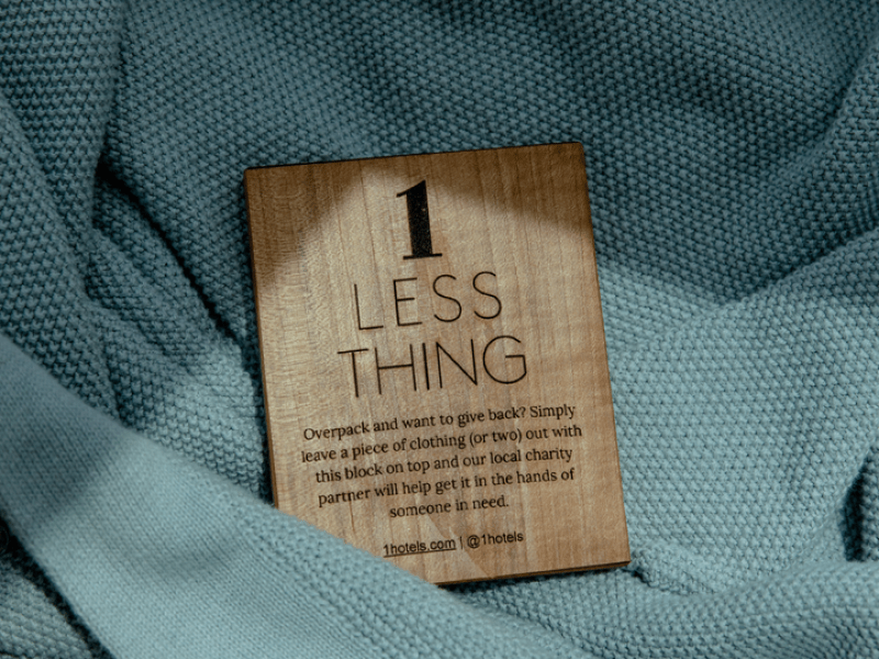 A wooden block with the text 1 Less Thing pictured nestled into a light blue sweater