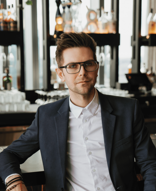 Person with glasses and a black suit resting at a bar