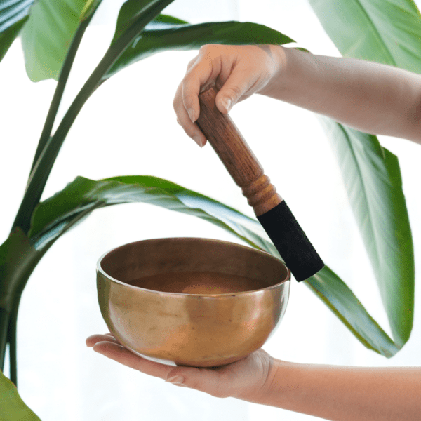 A hand holding a singing bowl, while another hand runs the mallet along the edge