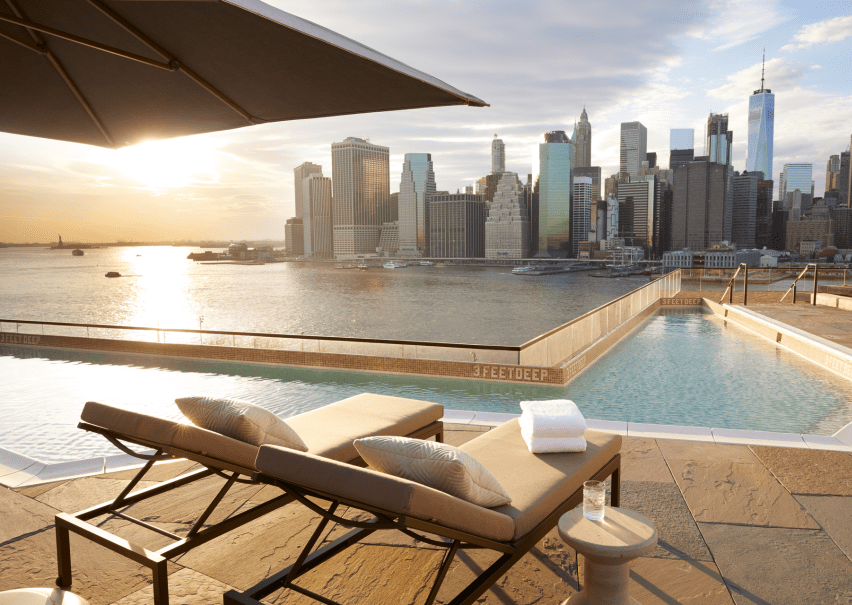 Relaxing rooftop pool area feautring reclined lounge chairs with a view of the skyline